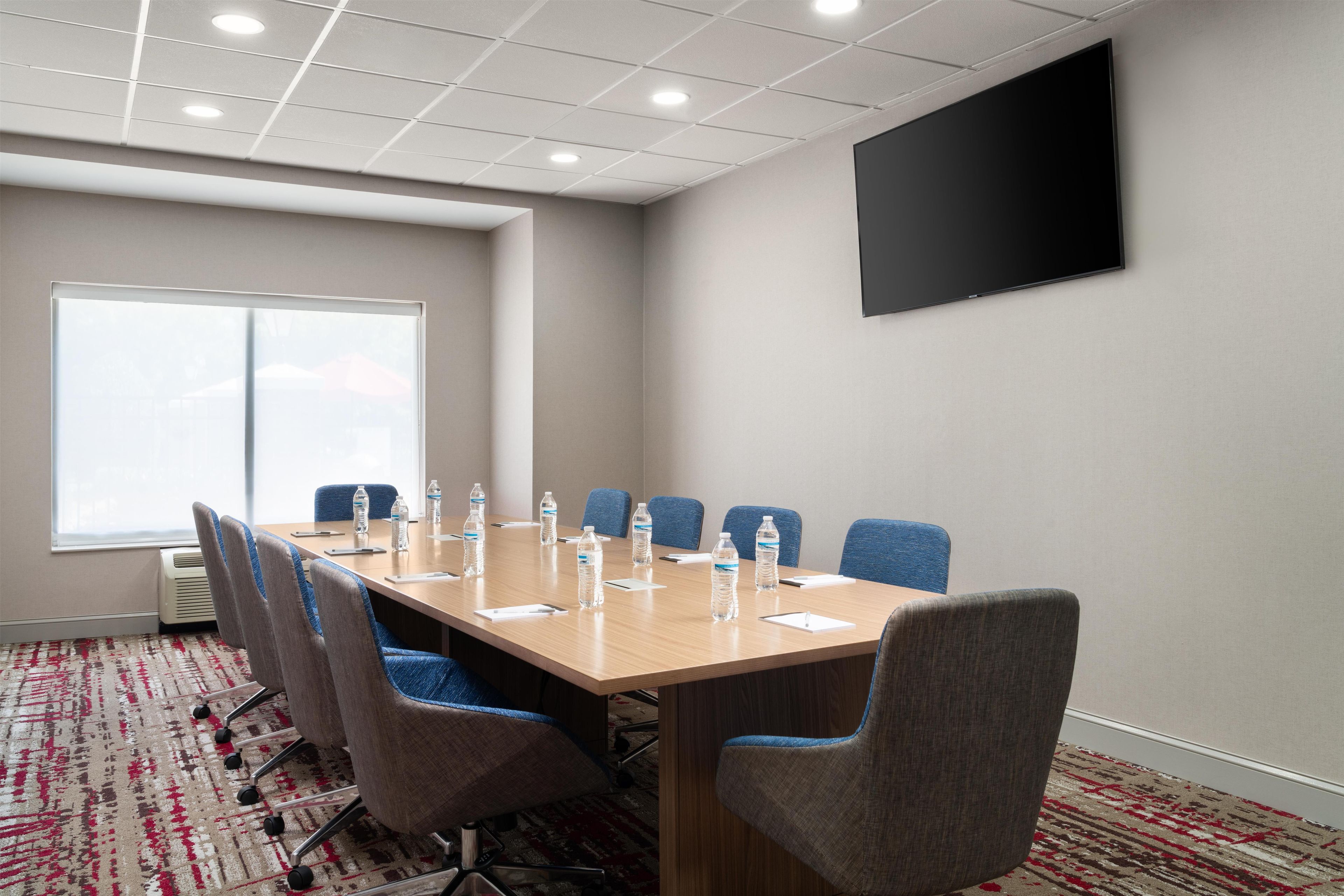 A conference room with a long table, six chairs, water bottles, and a flat-screen TV on the wall.