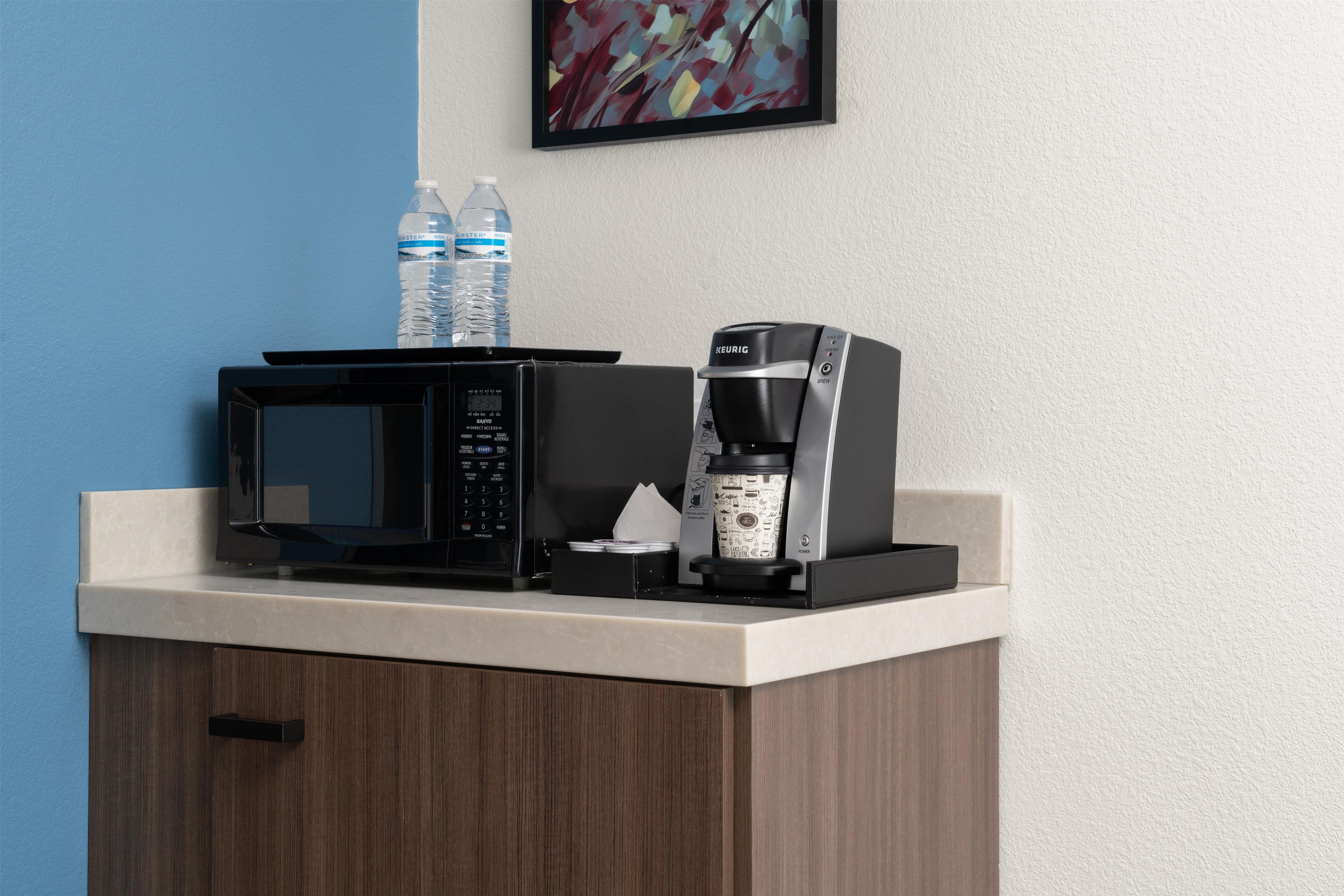 A kitchenette with a microwave, coffee maker, and water bottles on a countertop.
