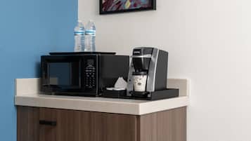 Eine Küchenzeile mit einer Mikrowelle, einer Kaffeemaschine und Wasserflaschen auf einer Arbeitsfläche.