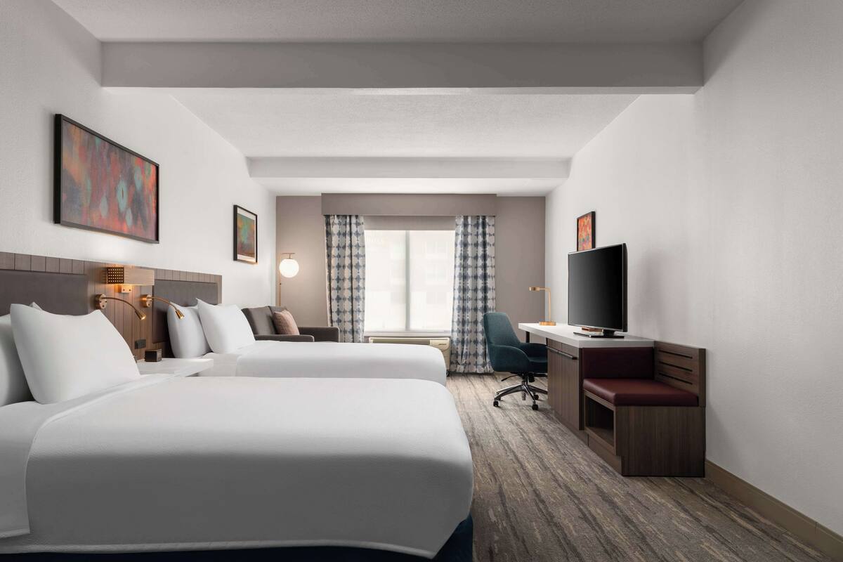 A hotel room with two beds, a desk with a TV, a chair, and a window with curtains.
