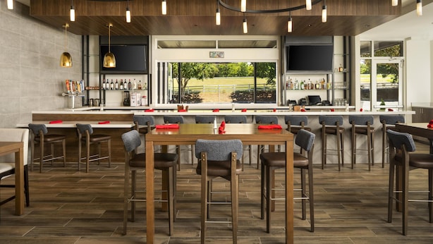A modern bar area with a long counter, multiple stools, and a view of a garden through large windows.