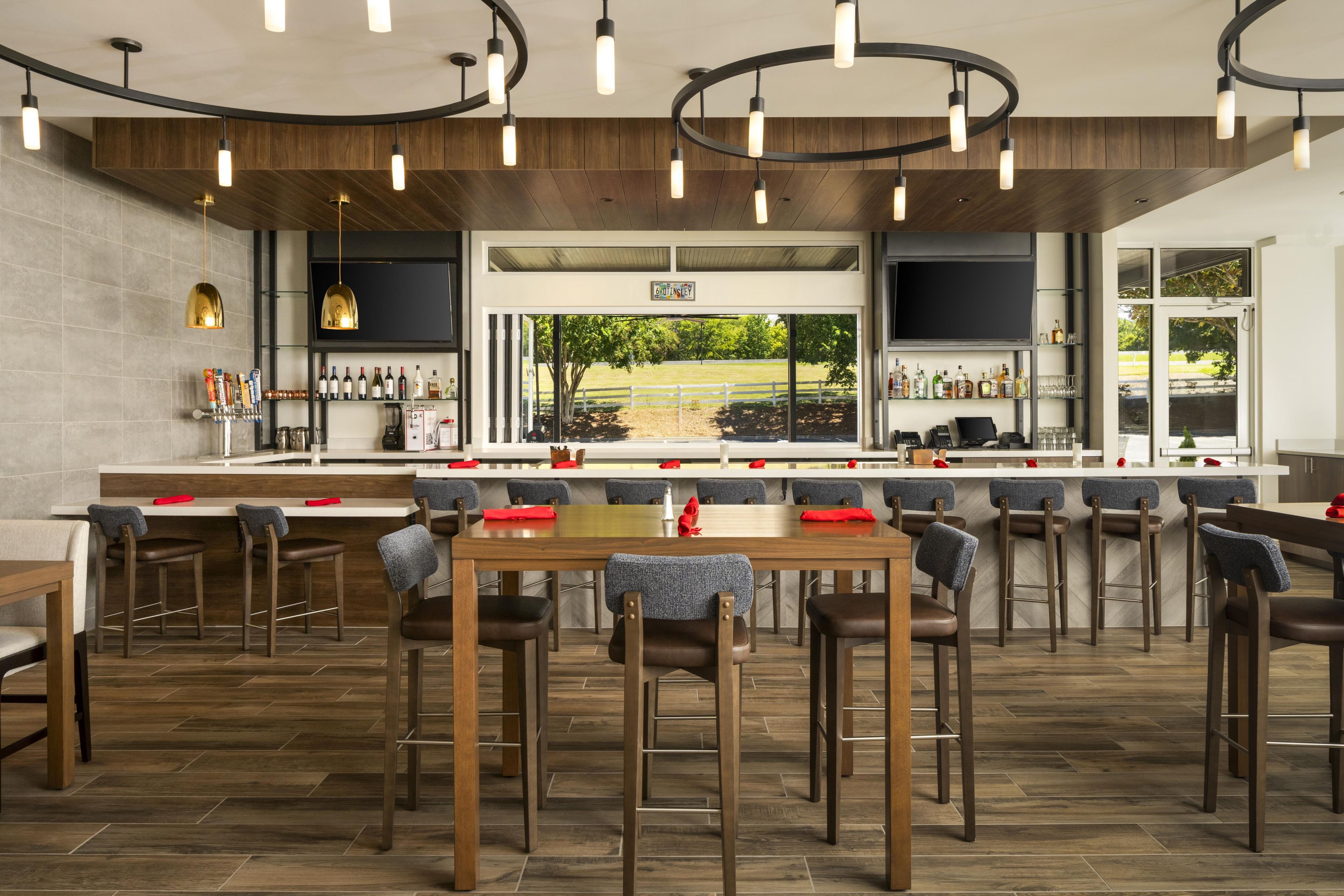 A modern bar area with a long counter, multiple seating options, and a view of the outdoors.