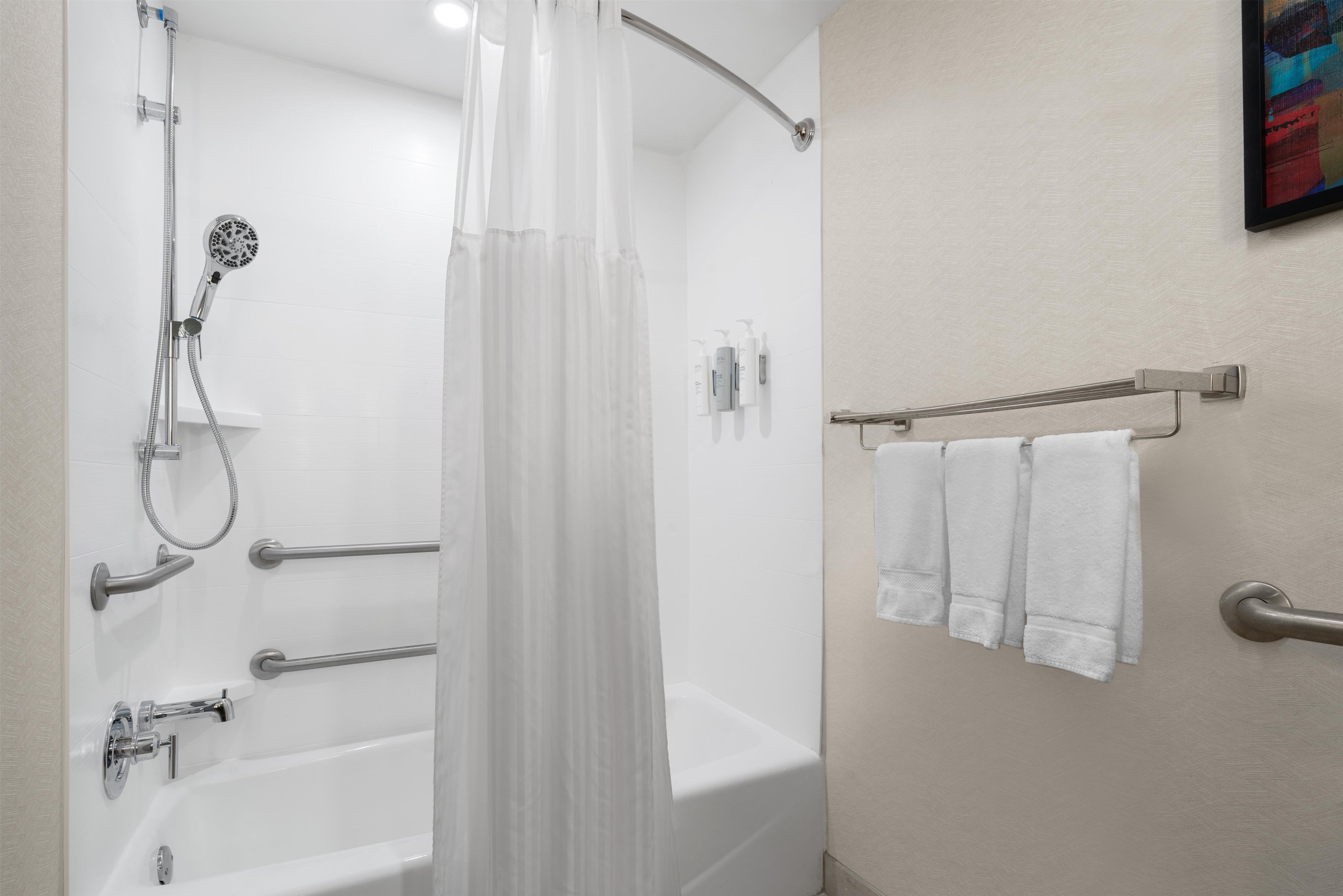 Un baño con bañera, ducha y barras de apoyo.