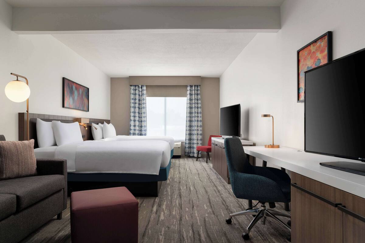 A hotel room with a large bed, a desk with a computer, a TV, a sofa, and a chair.
