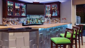 A bar area with a tiled backsplash, bar stools, and a variety of bottles and glasses. - Hilton Garden Inn Bridgewater (Bridgewater)
