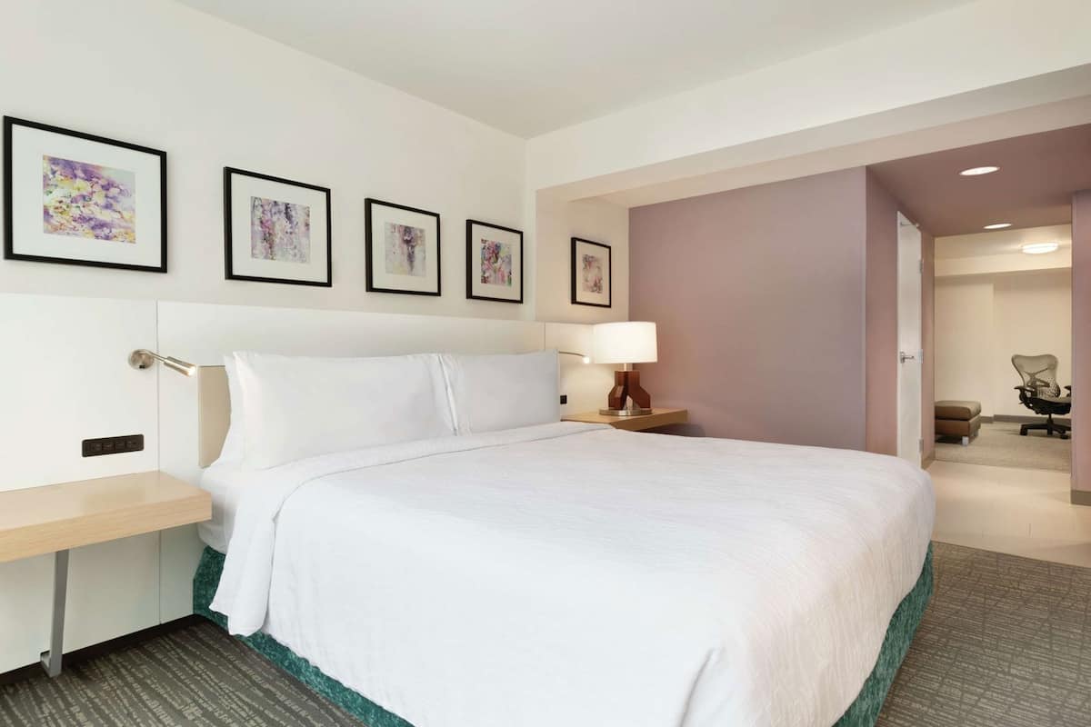 A hotel room with a large bed, a bedside table, a lamp, and framed artwork on the wall.