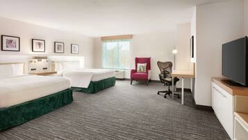 A hotel room with two beds, a desk, a chair, a television, and framed pictures on the wall.