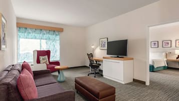 Une chambre d’hôtel moderne, dotée d’un canapé, d’un pouf, d’un fauteuil rouge, d’un bureau, d’une télévision et d’œuvres d’art accrochées aux murs.