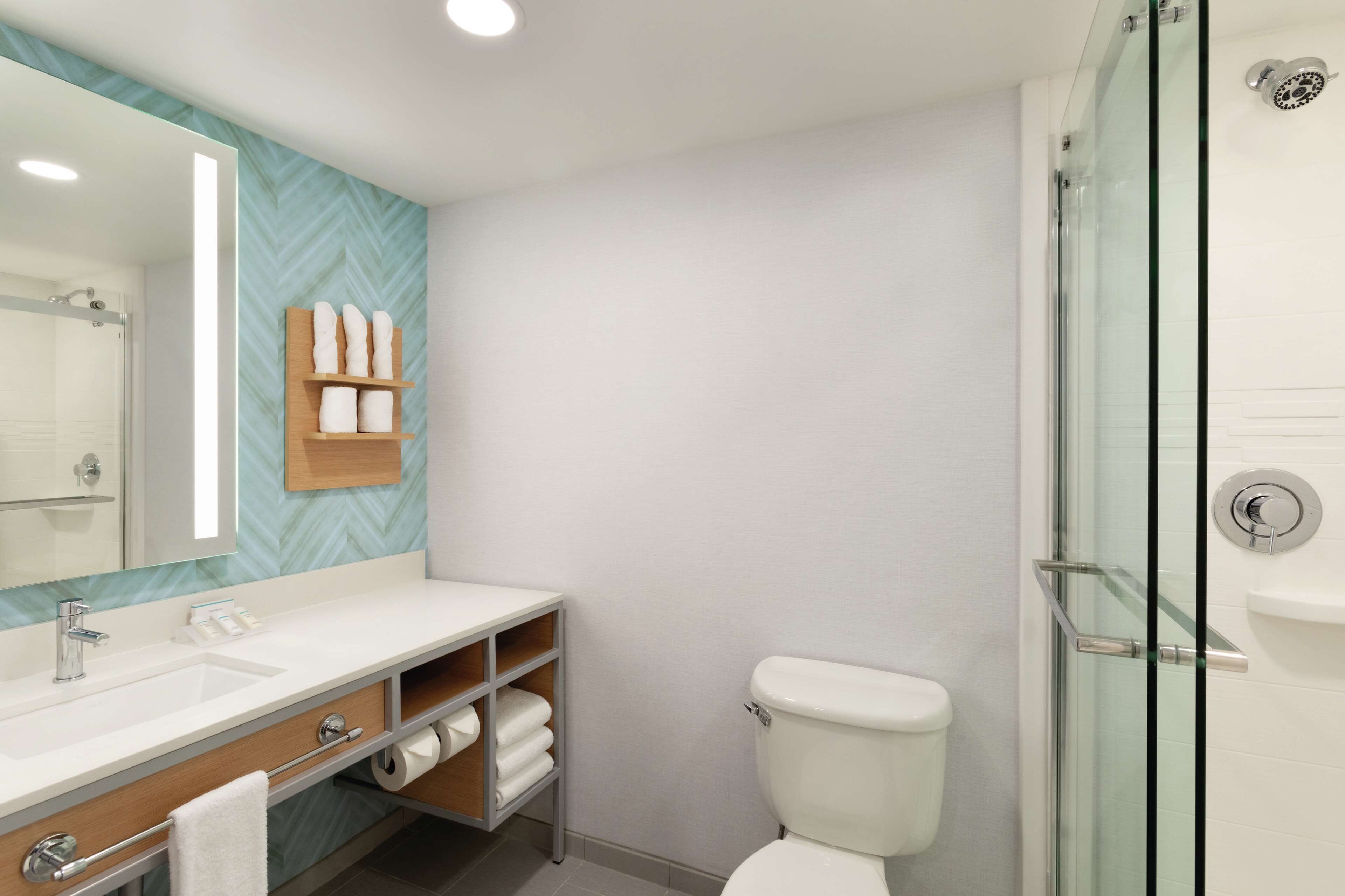 A modern bathroom with a large mirror, a white sink, a glass shower enclosure, and a toilet.