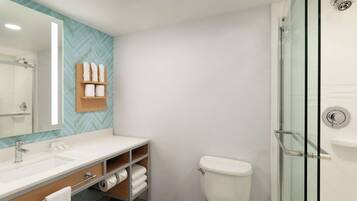 A modern bathroom with a large mirror, a white sink, a glass shower enclosure, and a toilet.