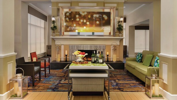A spacious living room with a fireplace, comfortable seating, and a television screen displaying a message. - Hilton Garden Inn Bridgewater (Bridgewater)