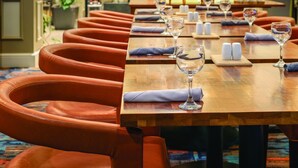A restaurant with a long wooden table set for dining, surrounded by leather chairs. - Hilton Garden Inn Bridgewater (Bridgewater)