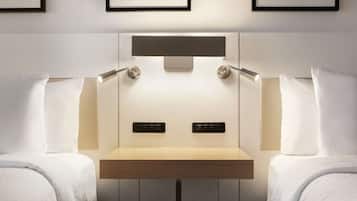 A hotel room with two beds, a bedside table, wall-mounted light, and framed artwork.
