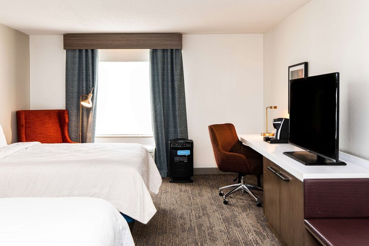 A hotel room with two beds, a desk with a TV, a chair, and a desk lamp.
