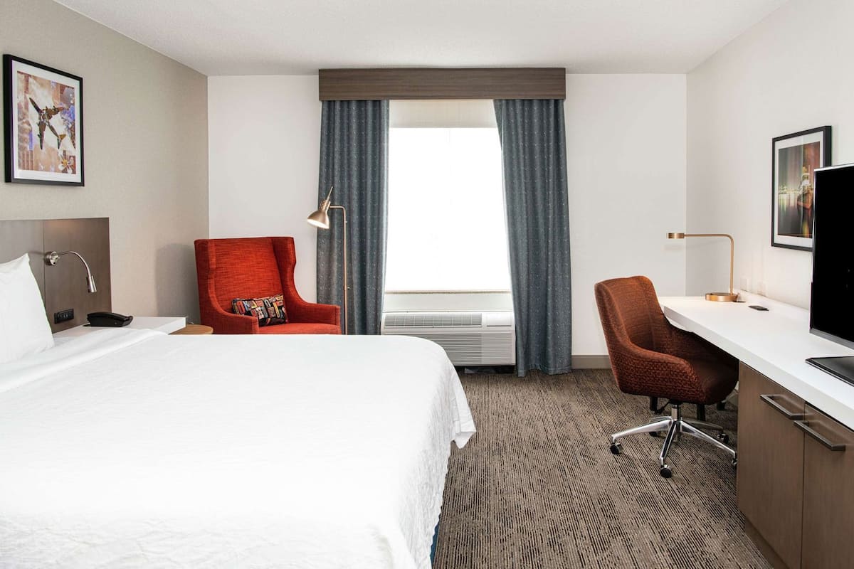 A hotel room with a bed, a desk, a television, a chair, and a window with curtains.