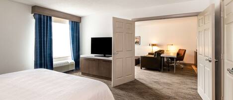 A hotel room with a bed, a desk with a computer, a television, and a door leading to another room.