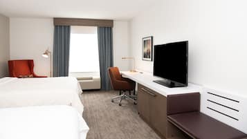 Une chambre d’hôtel avec deux lits, un bureau doté d’un téléviseur à écran plat, un fauteuil rouge et une grande fenêtre avec des rideaux.