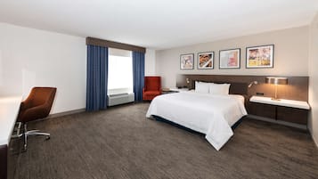 Habitación de hotel con una cama grande, un escritorio con lámpara, una silla y una ventana con cortinas.