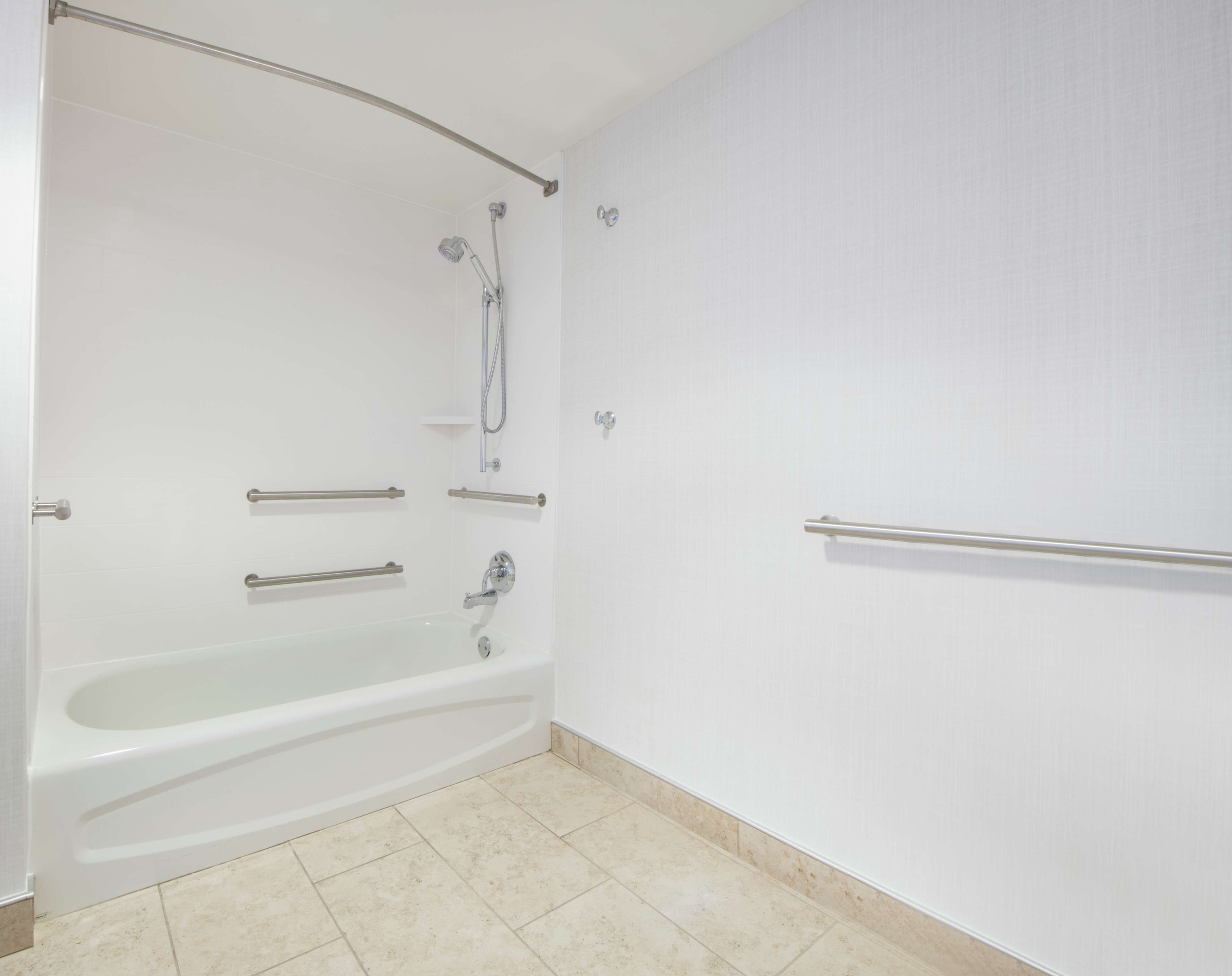 Un baño con una bañera blanca, ducha y barras de apoyo.