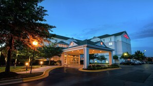 A hotel entrance with a covered lobby, a parking area, and a Hilton Garden Inn sign.