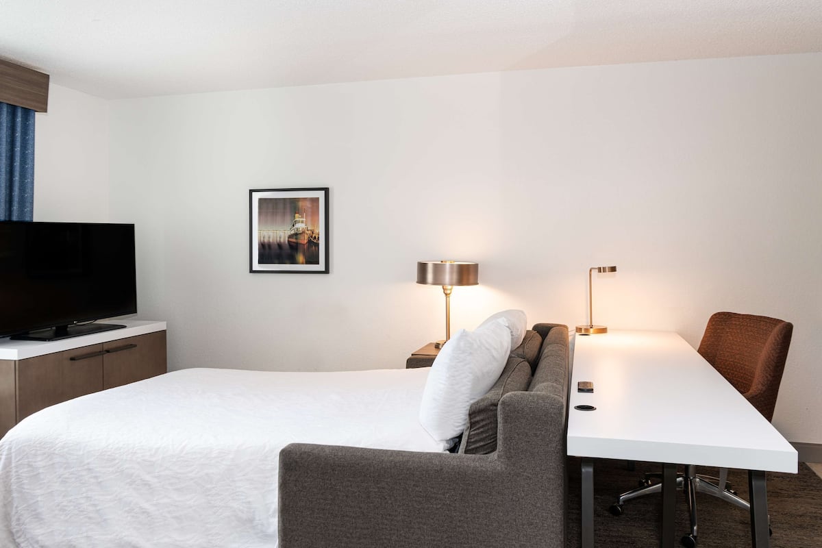 A hotel room with a bed, a TV, a desk with a chair, and two lamps.