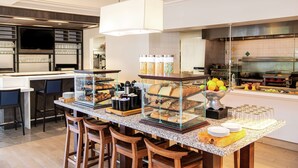 A breakfast bar with various food items, a coffee station, and a kitchen area in the background.