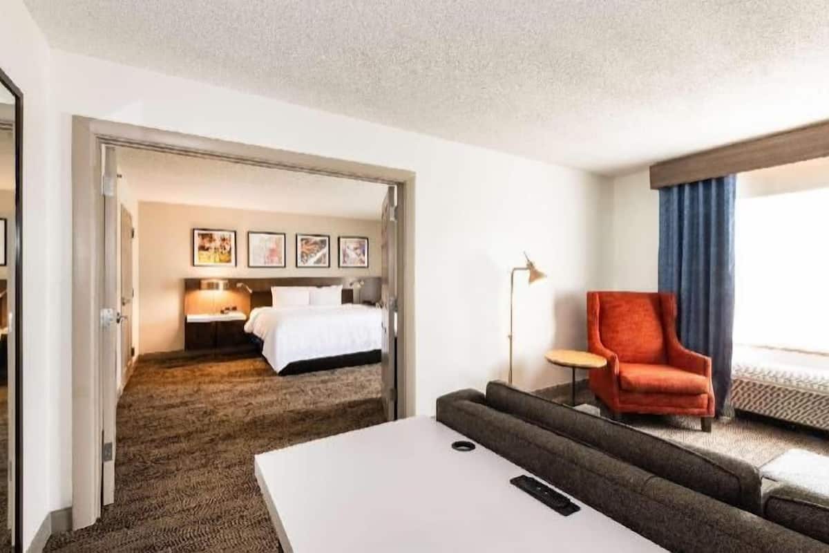 A hotel room with a bed, a sofa, a chair, a desk, and a large window.