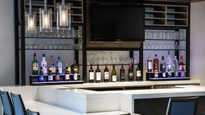A bar area with a long counter, multiple liquor bottles, glasses, and a flat-screen TV mounted above.