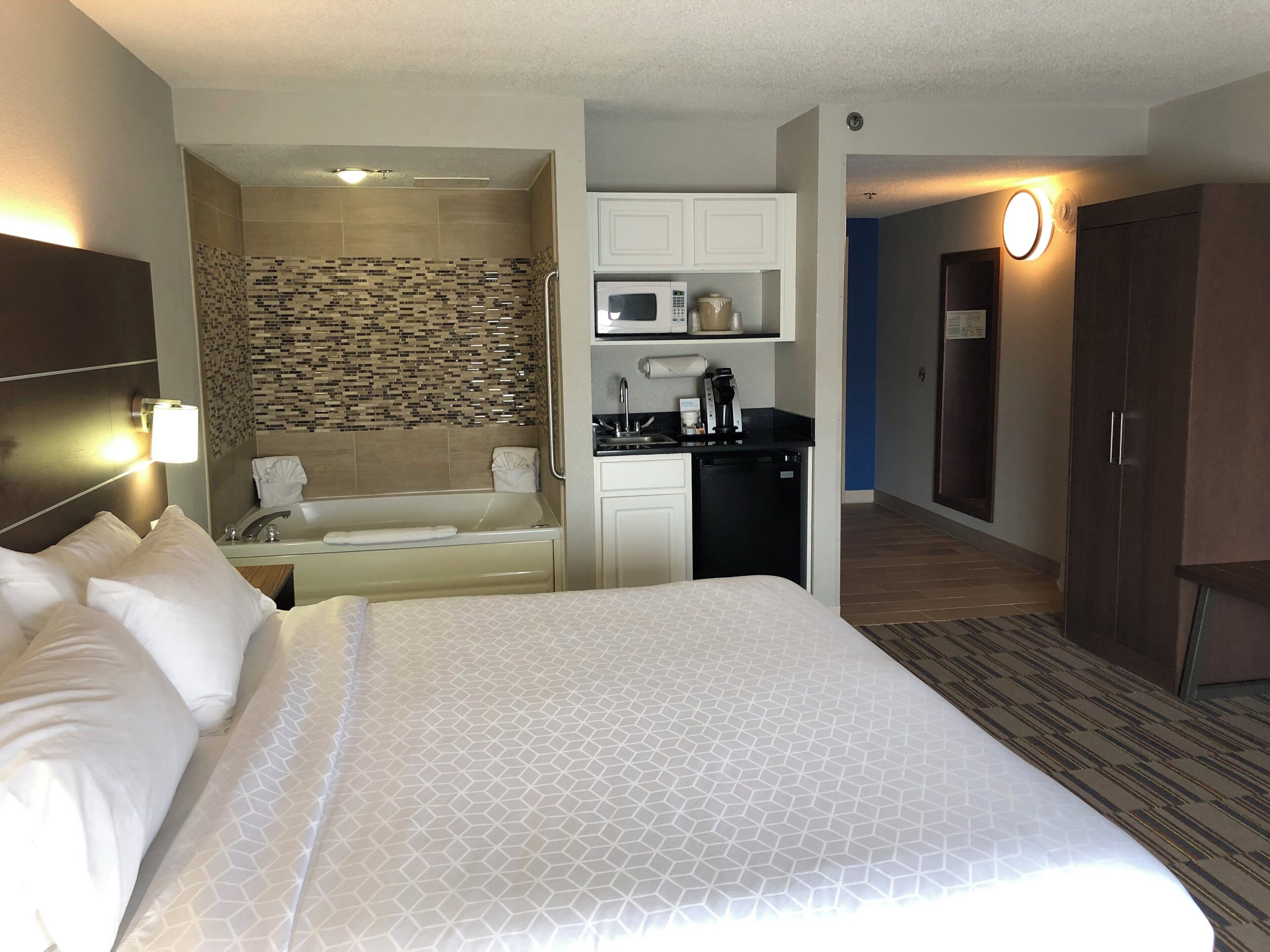 A hotel room with a large bed, a kitchenette, a shower area, and a walk-in closet.