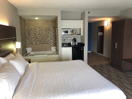 A hotel room with a large bed, a kitchenette, a shower area, and a walk-in closet.