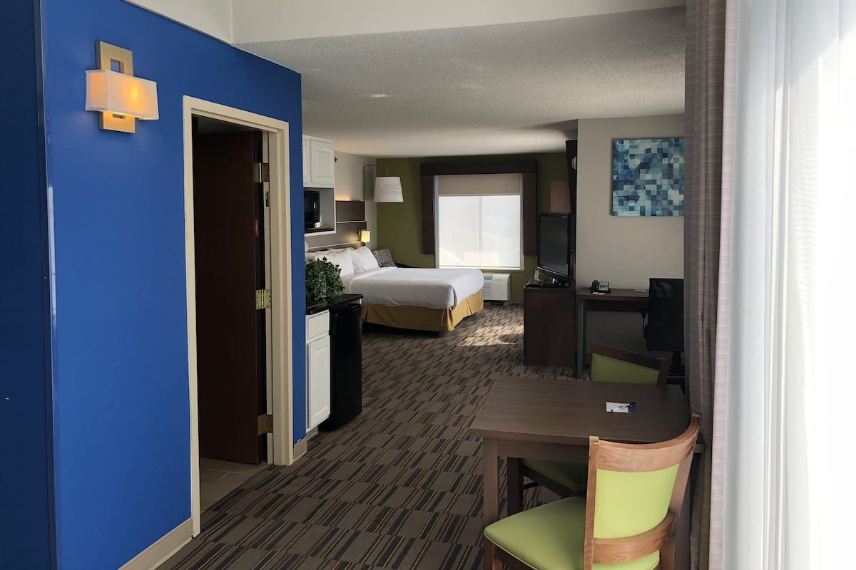 A hotel room with a bed, desk, chair, and a large window.