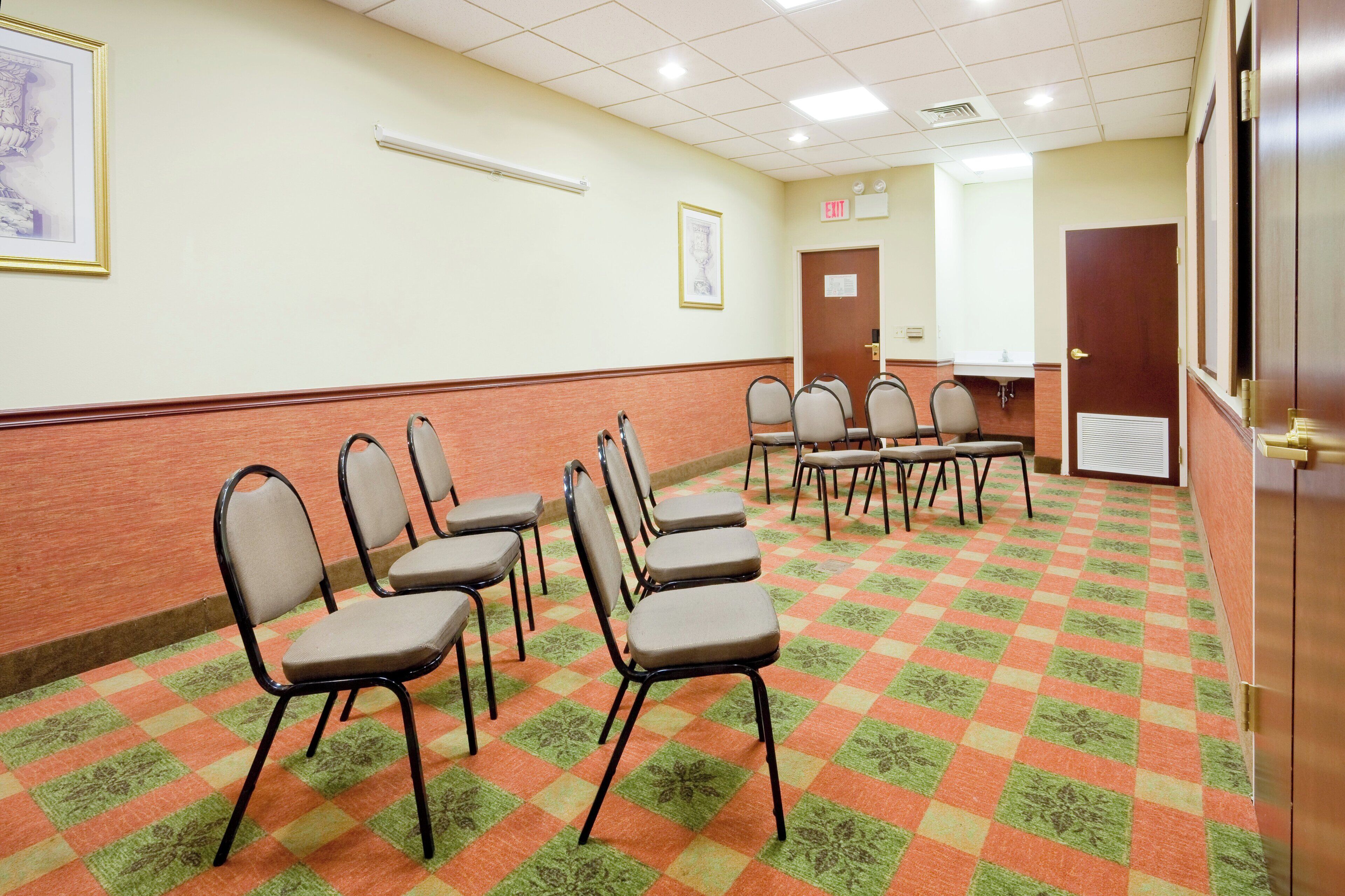 Une salle de conférence avec des rangées de chaises, une porte et un panneau indicateur de sortie fixé au mur.