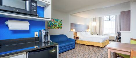 Habitación de hotel con kitchenette, una cama, un sofá azul, una mesa de comedor y un cuadro en la pared.
