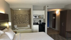Camera d'albergo con un letto grande, angolo cottura, bagno con doccia e cabina armadio.
