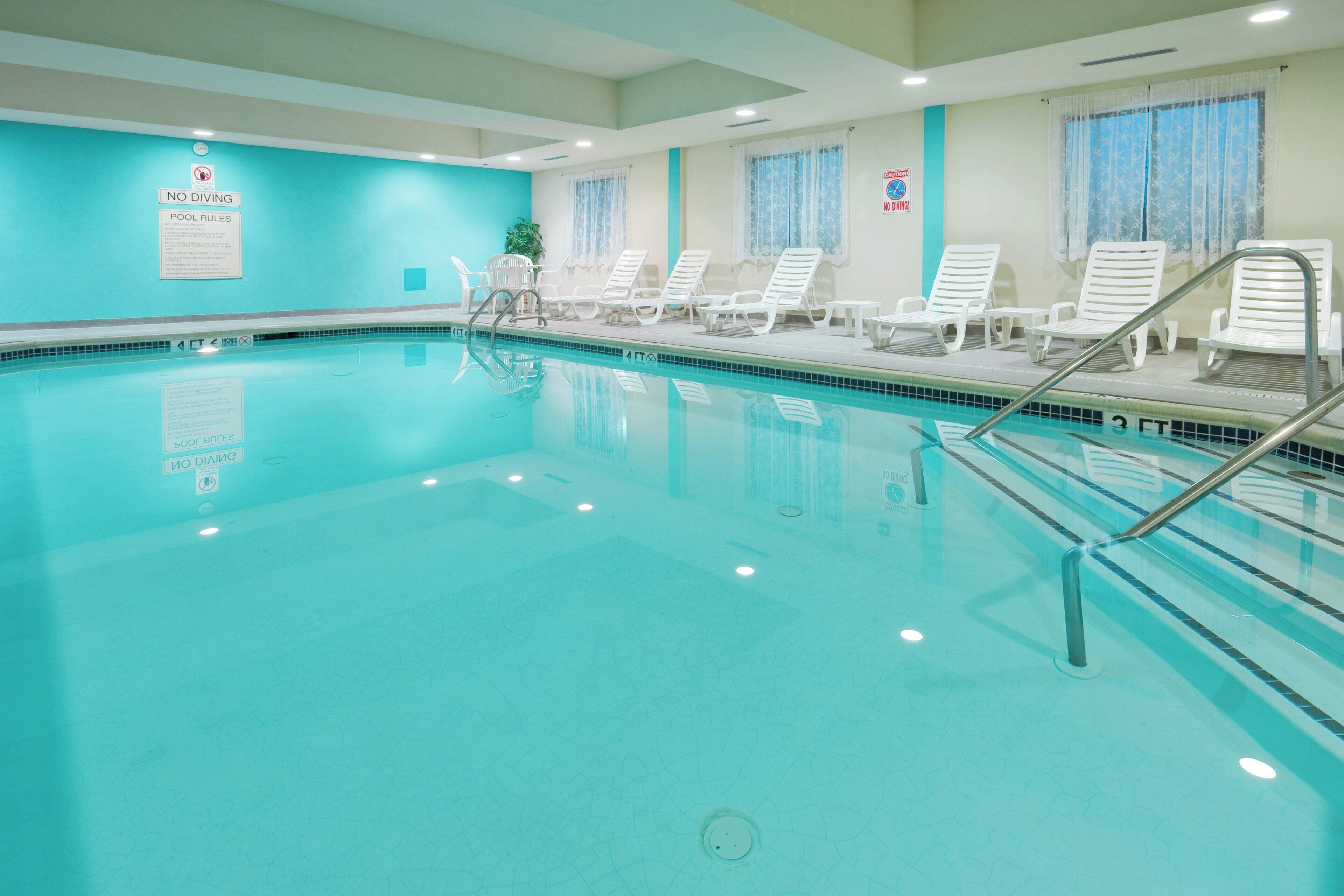 Une piscine intérieure à l’eau claire, avec un escalier et des chaises longues disposées le long du bord.
