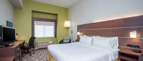 Quarto de hotel com uma cama grande, uma escrivaninha com computador, uma cadeira e uma televisão.