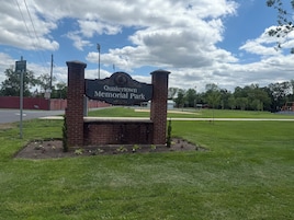 A sign for Quakertown Memorial Park with a brick base and a green field in the background.