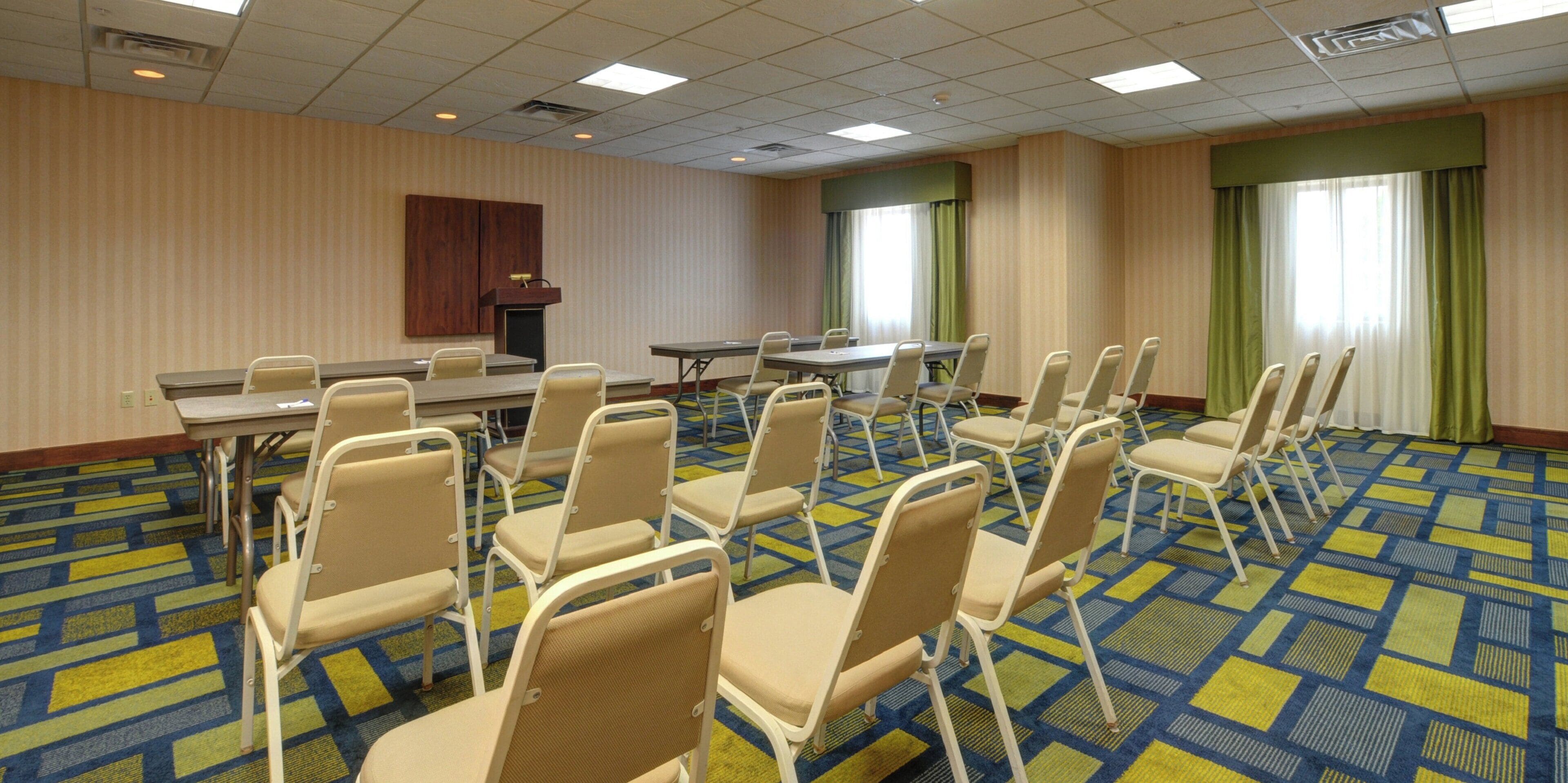 Un salón de conferencias con una gran mesa, varias sillas, un atril y suelo alfombrado.