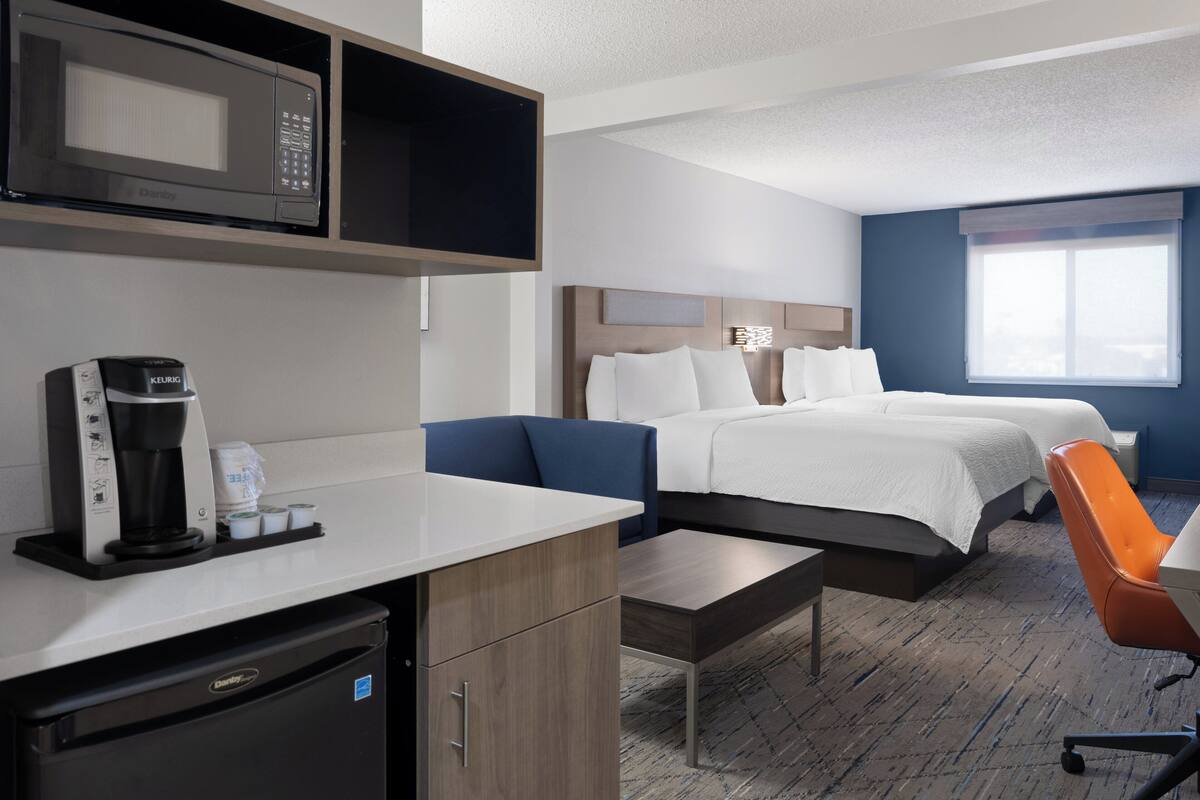 A hotel room with a bed, a desk, a microwave, a coffee maker, and a chair.