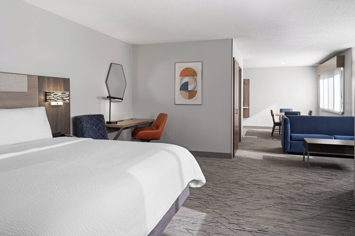 A hotel room with a large bed, a desk with a chair, a sofa, and a large window.