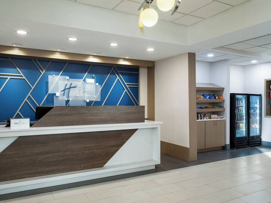 Un espace d’accueil au design moderne, comprenant un comptoir de réception, un mur bleu et blanc orné de motifs géométriques, et un réfrigérateur rempli de boissons.