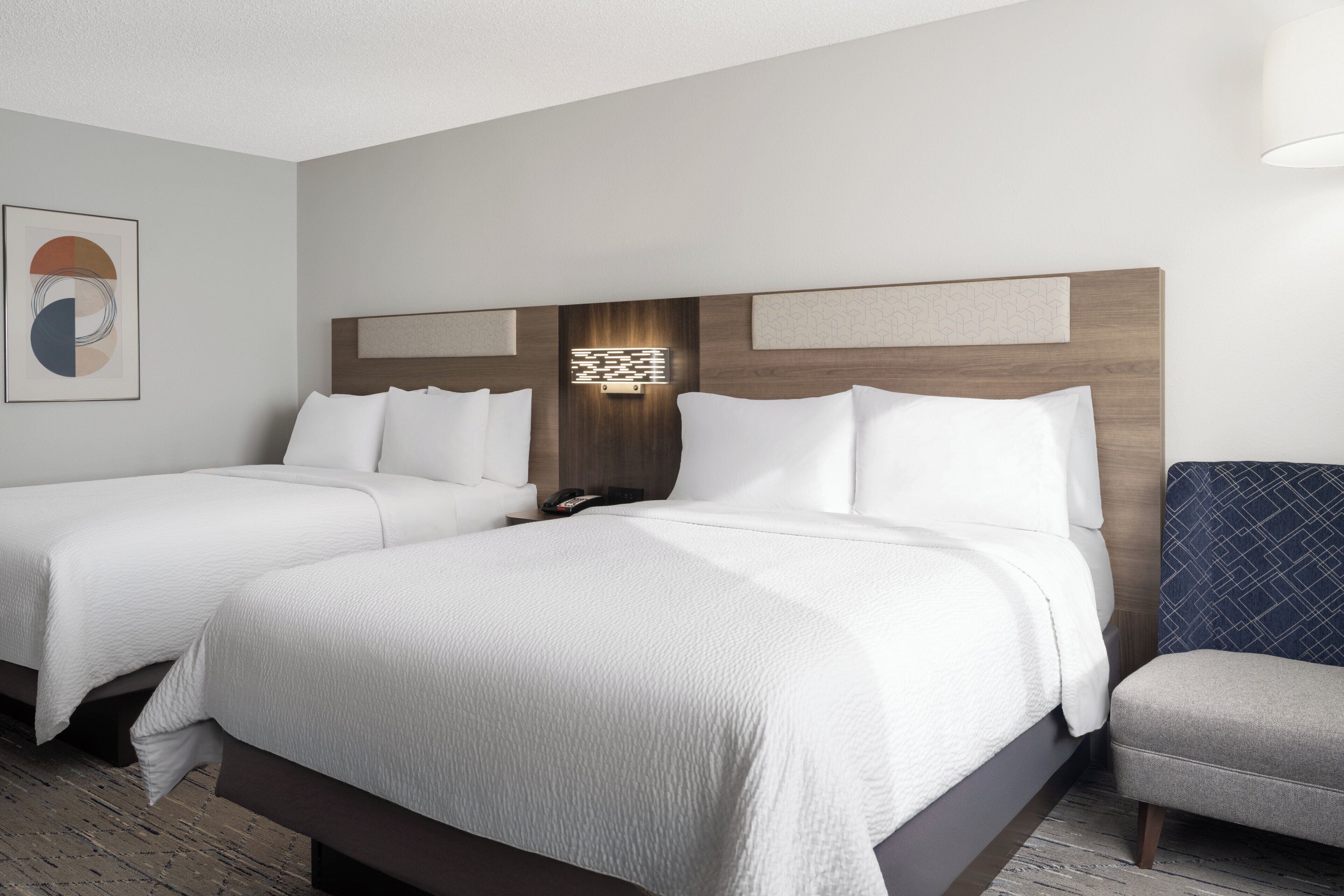 Habitación de hotel con dos camas, una mesita de noche, una lámpara y un cuadro en la pared.