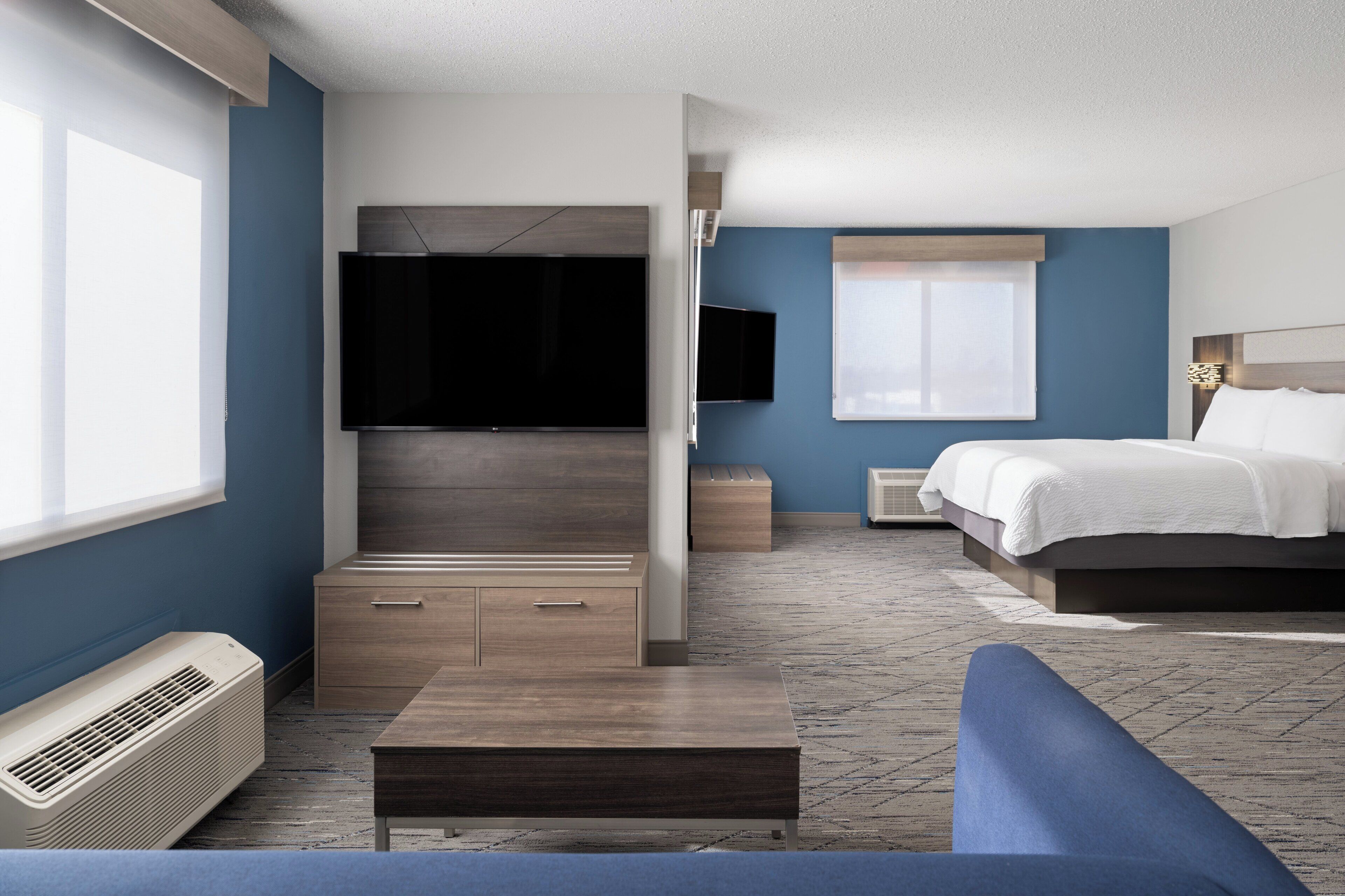 A modern hotel room with a large flat-screen TV, a bed, a sofa, and a small table.