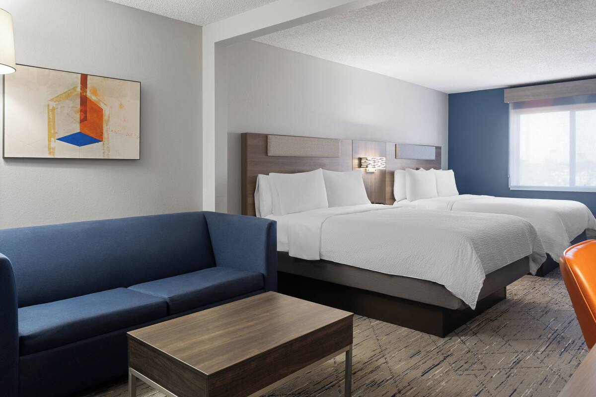 A hotel room with a bed, a blue sofa, a wooden table, and a painting on the wall.