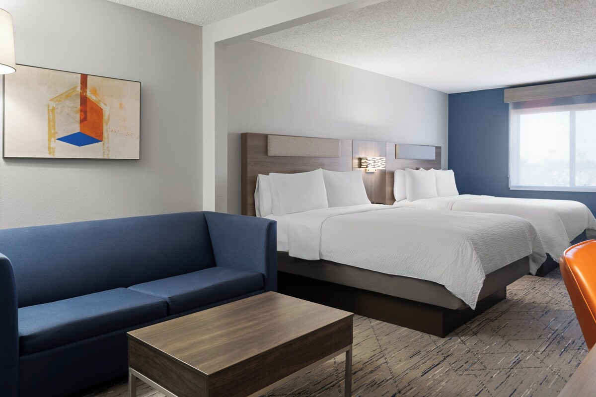 A hotel room with a bed, a blue sofa, a wooden table, and a painting on the wall.