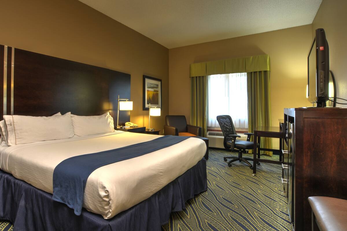 A hotel room with a large bed, a desk with a chair, a TV, and a window with curtains.