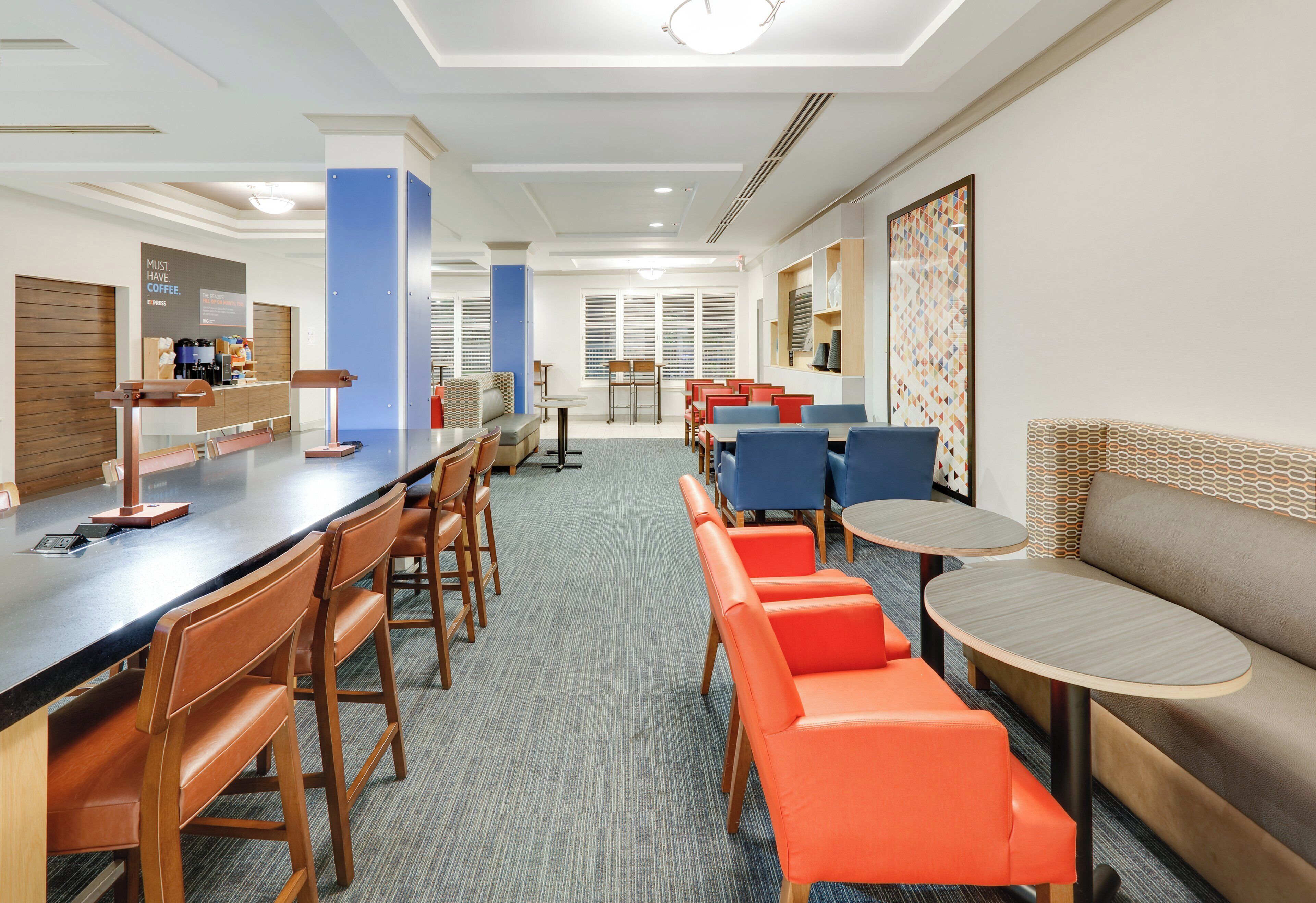 Un espace de restauration d’hôtel doté d’un long comptoir, de plusieurs options de sièges, notamment des banquettes et des tables, ainsi que d’un coin café.