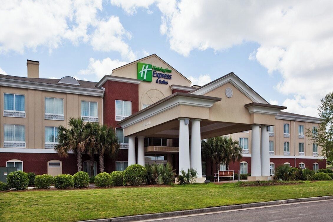A Holiday Inn Express & Suites hotel with a covered entrance, multiple windows, and a well-maintained lawn.