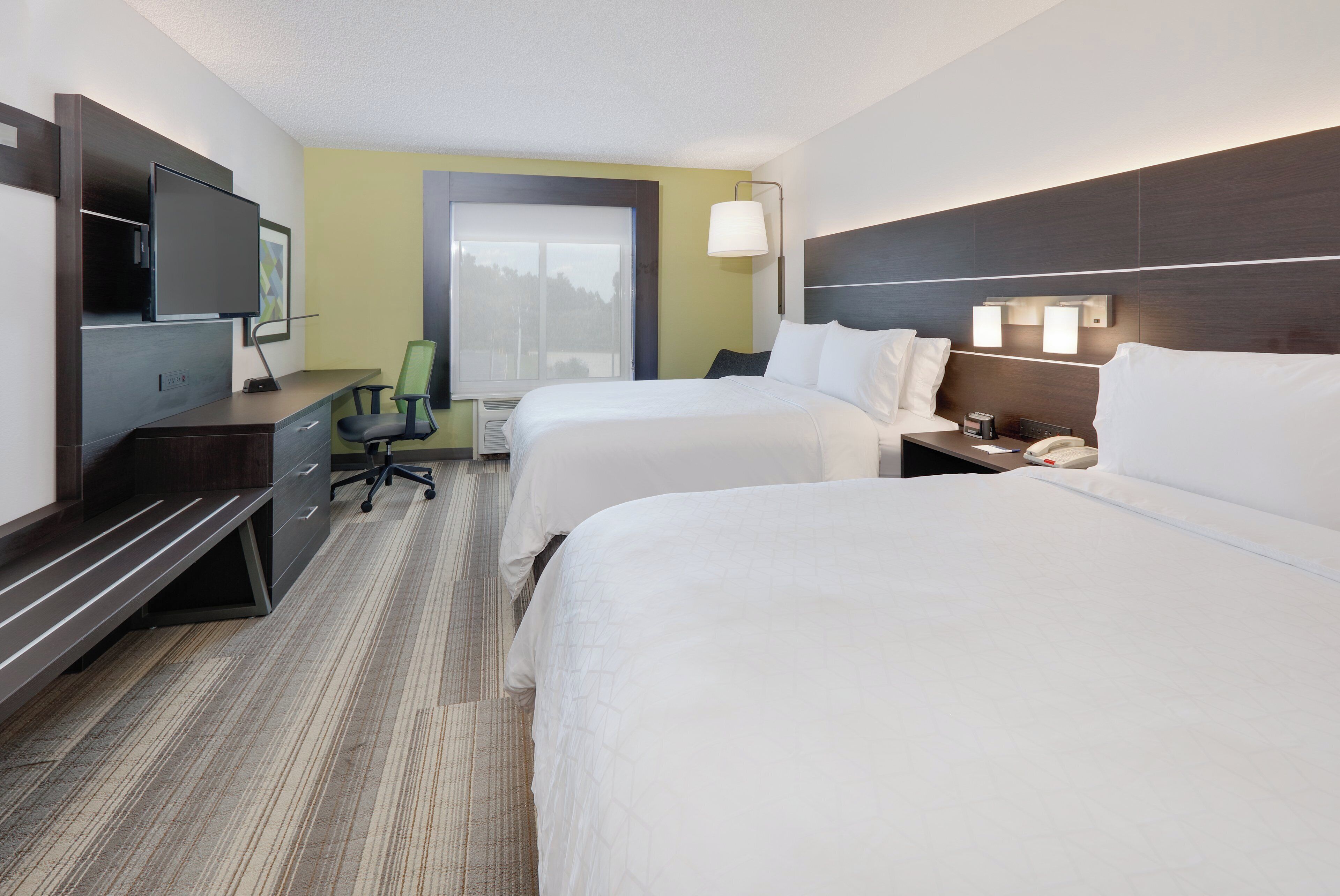 A hotel room with two beds, a desk, a chair, a television, and a window.