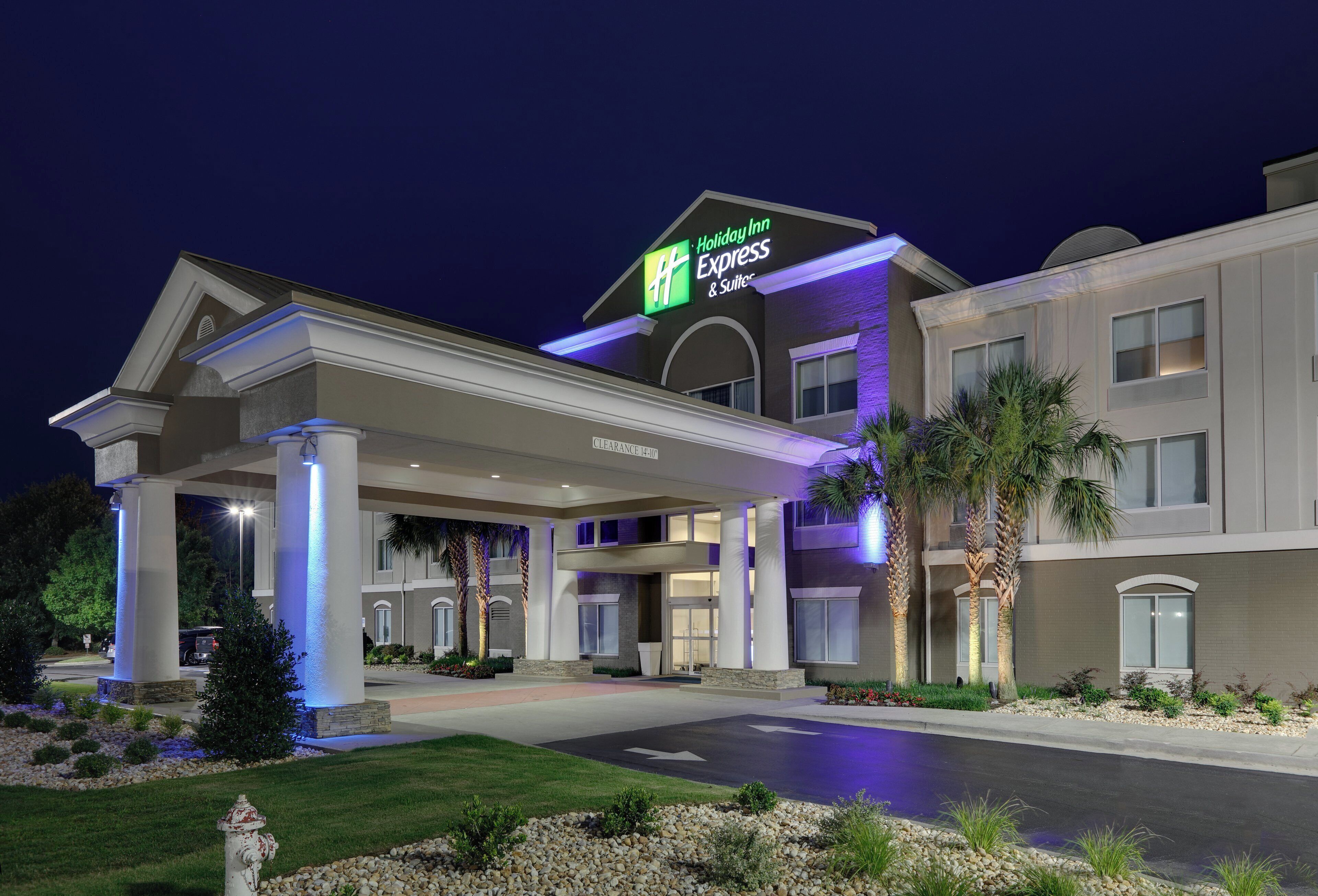 A Holiday Inn Express & Suites building with a clear entrance, a covered parking area, and a landscaped front yard.